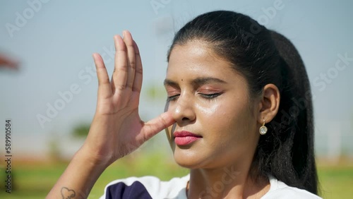 Close up head shot of woman doing nostril breathing or pranayama yoga or exercise with eyes closed at park - concept of calmness or relaxation, rejuvenation and photo