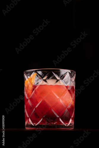 negroni cocktail seen from above with round orange ice on wooden table from the front with isolated black background © mario