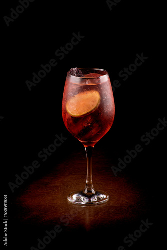 refreshing glass of lillet spritz aperol cocktail with lime and ice on wooden table with dark background seen at angle