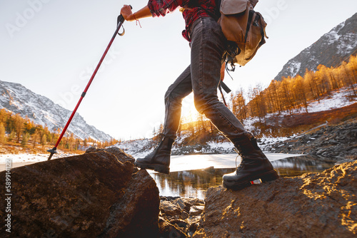 Young girl walks with backpack and hiking poles against mountain lake and sunset