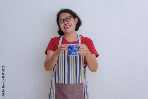 A woman wearing apron over red t-shirt hold a bluish cup with both her hands, smiling, happy. photo