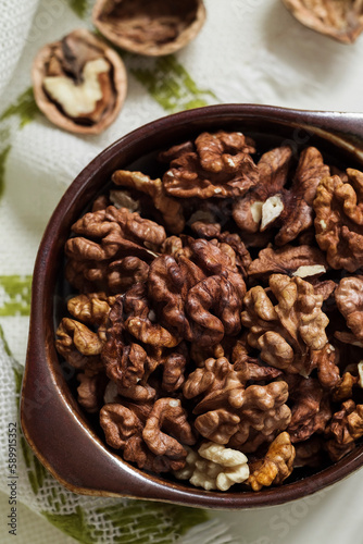Fresh organic walnut kernels close up in a brown ceramic bowl. Top view.