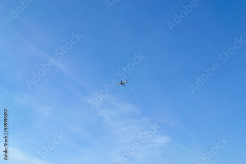 The plane flies high in the blue sky with small clouds