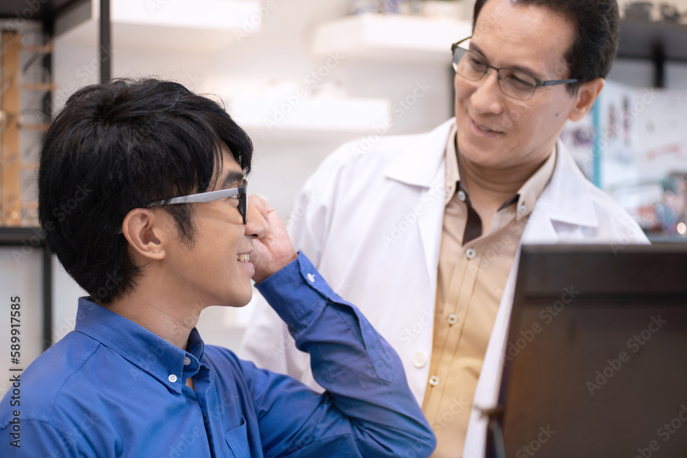 Happy young male client trying out new eyeglasses with expert advice, look at each other, Asian man holding and trying on new spectacles Happy young male client trying out new eyeglasses with expert advice, look at each other, Asian man holding and trying on new spectacles