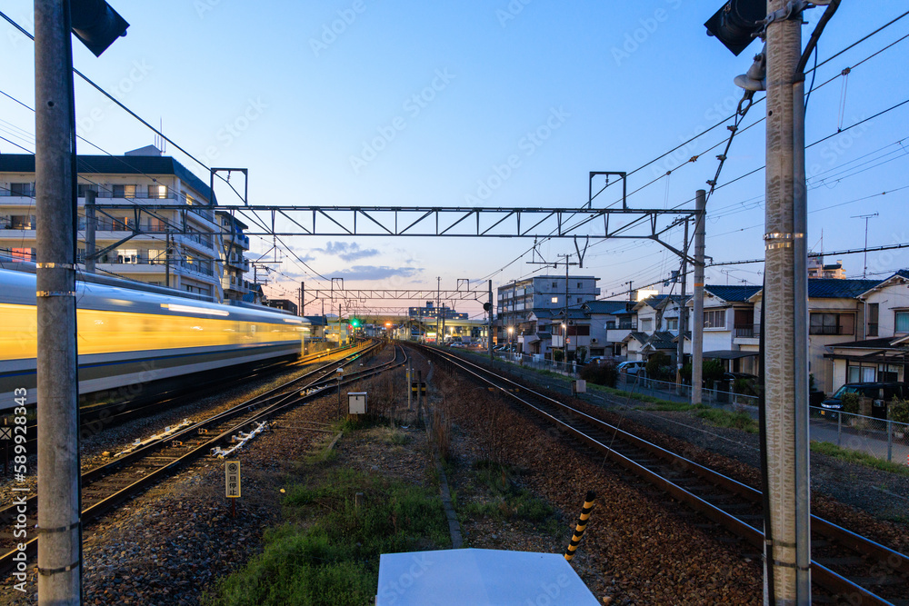 Fototapeta premium Fast moving train blurs down tracks by homes in residential neighborhood at sunset