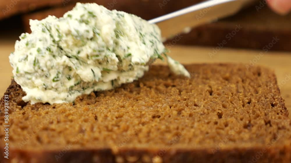 Cream cheese spread with fresh herbs is spread with a knife on a piece of rye bread. Cream cheese spread with fresh herbs is spread with a knife on a piece of rye bread.