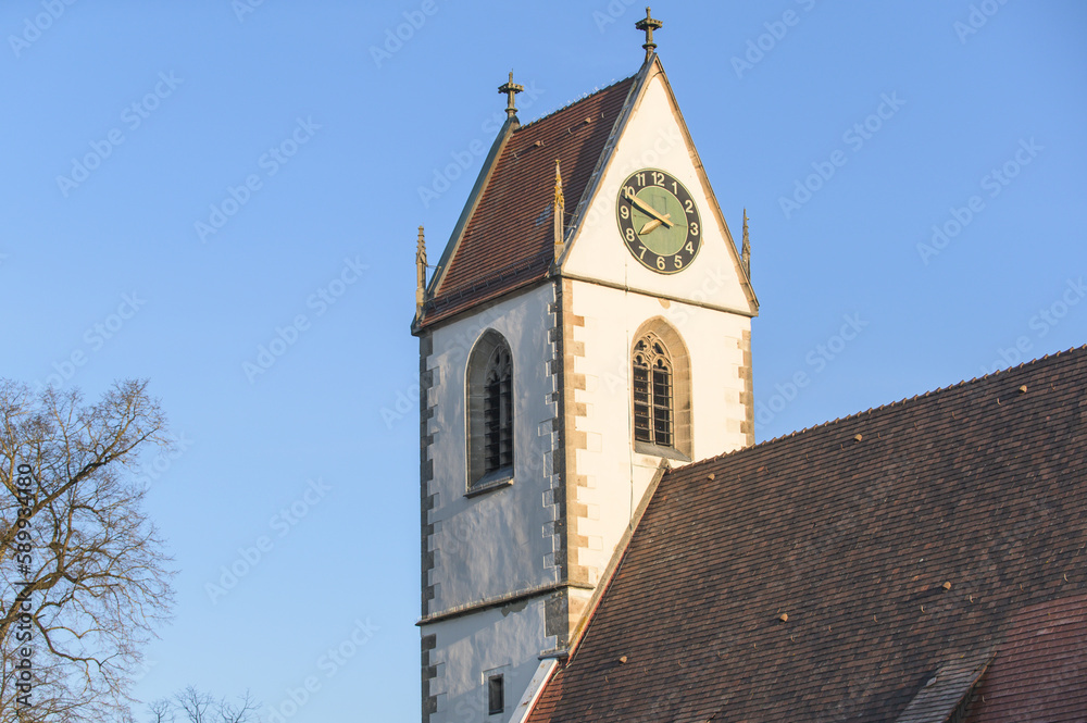 Kirchturm mit gotischen Fenstern und Kirchturmuhr im Streiflicht vor blauem Himmel