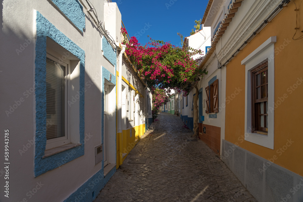 Beautiful Luiz Antonio dos Santos street of the fishing village of Ferragudo at sunset with its typical white, blue and yellow facades of the houses and beautiful flowers, Algarve region, Portugal.