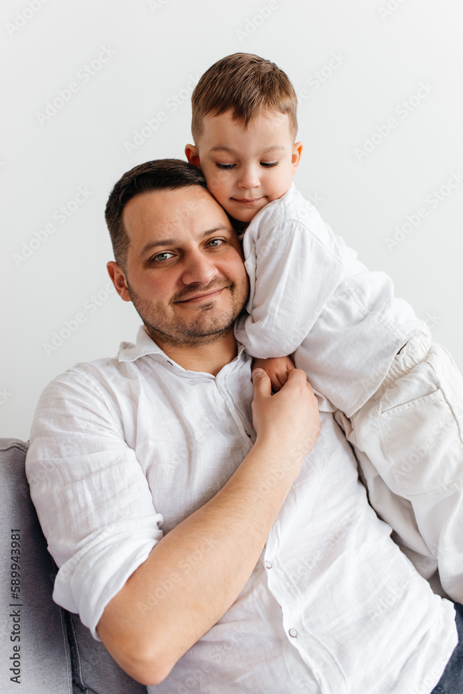 Mature father with small son sitting on sofa indoors, resting.