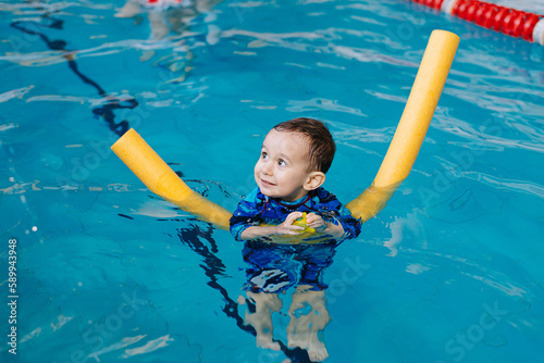 Happy little boy learning to swim with pool noodle