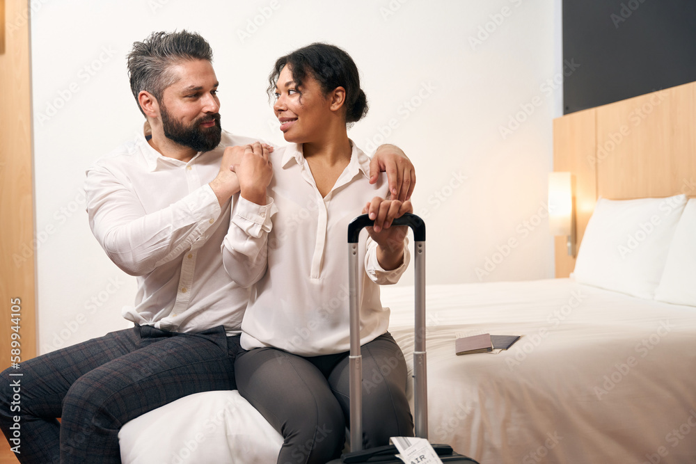 Couple in love seated with baggage in hotel room Couple in love seated with baggage in hotel room
