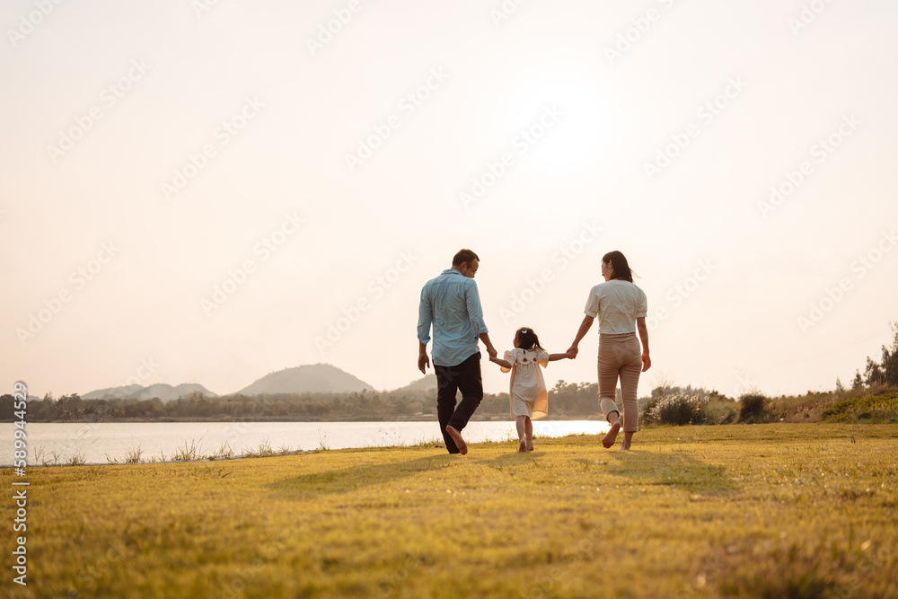 Happy Family enjoying a peaceful walk and running in a scenic field with a serene lake in the background.