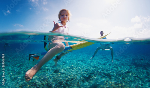 Boy surfs with his father. Preteen boy sits on the surf board in the tropical ocean with his family