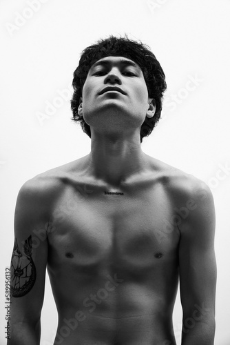 Black and white image of young athletic guy posing with eyes closed, shirtless againtshite background. Inner world, mind opening. Concept of male body aesthetics, style, fashion, health © master1305