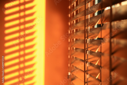 Abstract orange background. Wooden blinds illuminated by the setting sun in blurred focus. 
Bright sunset light coming through the window blinds.