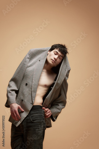 Portrait of young asian guy, boy wearing grey jacked at naked torso, position against studio background. Feeling style. Concept of male body aesthetics, style, health, men's beauty and fashion