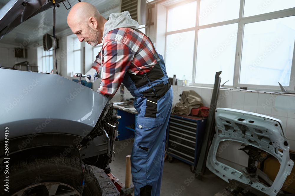 Auto repairman at the workplace repairs a car