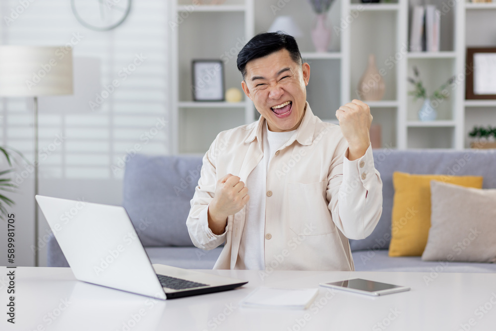 Asian working remotely from home office with laptop, businessman received notification of good achievement results, freelancer satisfied with work rejoices and celebrates victory and triumph. Asian working remotely from home office with laptop, businessman received notification of good achievement results, freelancer satisfied with work rejoices and celebrates victory and triumph.