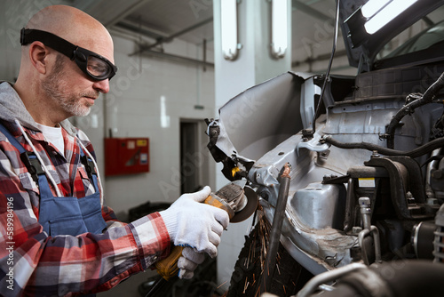 Worker in goggles uses pneumatic cutter to repair a car