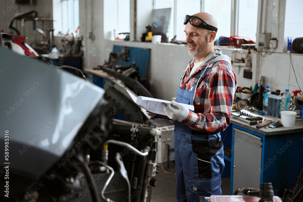 Satisfied man stands in workshop with working documentation in his hands Satisfied man stands in workshop with working documentation in his hands