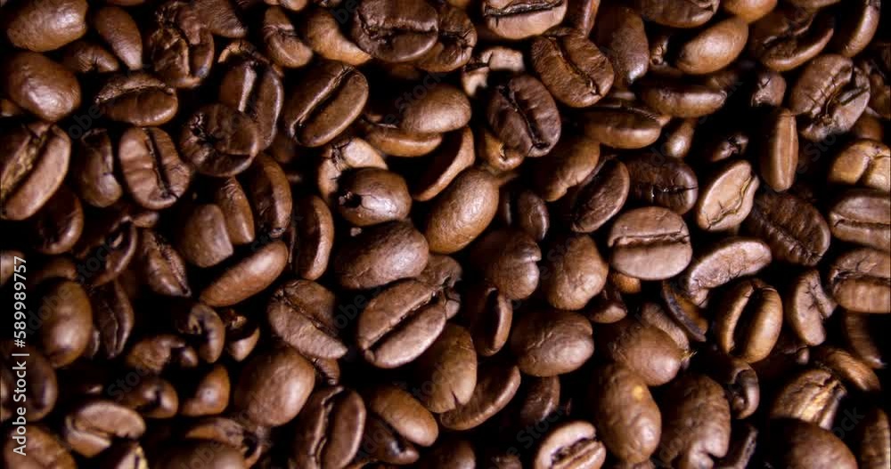 Roasted coffee beans close-up. Grains the coffee pours out and swirls in the container. A delicious hot drink product. Brown texture of coffee beans.
