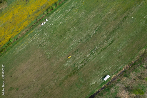 Top view of a yellow retro car on the summer green meadow field with white flowers and coils of hay distant plan