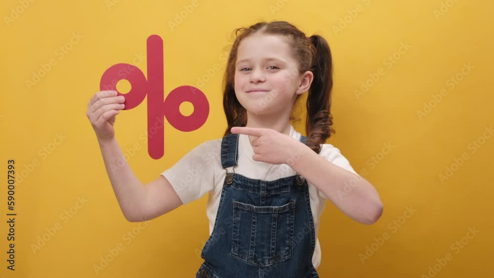 Portrait of pleasant happy little girl kid holding red percent mark, expressing positive emotions, presenting discounts, posing isolated over yellow color background wall in studio. Sale concept Portrait of pleasant happy little girl kid holding red percent mark, expressing positive emotions, presenting discounts, posing isolated over yellow color background wall in studio. Sale concept