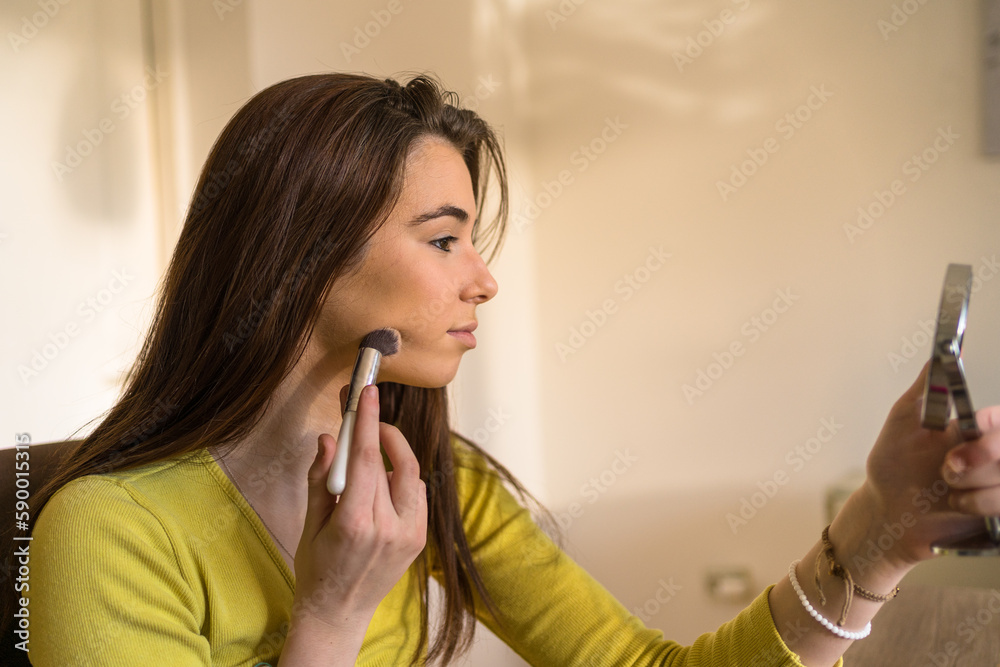 Young teenage woman doing make up in her living room, using her make up brush. Young teenage woman doing make up in her living room, using her make up brush.