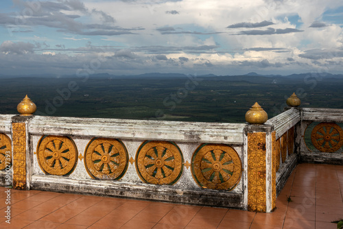 A beautiful decorative stone fence - parapet at the pagoda above the endless green tropical valley. Cloudy blue sky over the valley