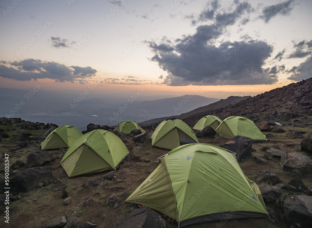 Tent camp of green identical tents on the rocky slope of Mount Ararat at sunset, identical tents a team of tourists on the ascent