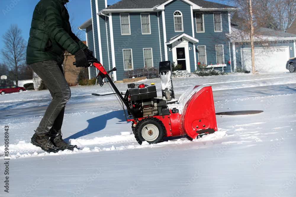 A man  is cleaing  snow from sidewalks with a snowblower after a snowstorm.