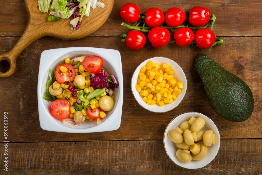 salad with lettuce and cherry tomato with avocado olive oil in a white plate on a wooden table next to all the ingredients. salad with lettuce and cherry tomato with avocado olive oil in a white plate on a wooden table next to all the ingredients.