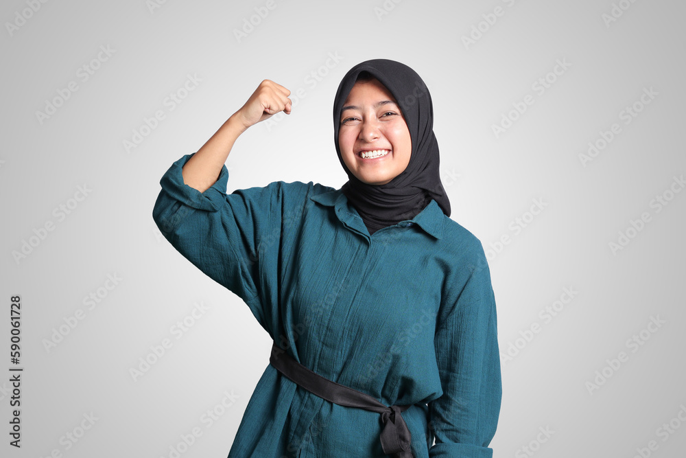 Portrait of excited Asian muslim woman with hijab raising her fist, celebrating success. Advertising concept. Isolated image on white background Portrait of excited Asian muslim woman with hijab raising her fist, celebrating success. Advertising concept. Isolated image on white background
