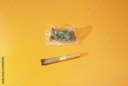 Cigarro porro y bolsita de plástico con marihuana en su interior sobre fondo rugoso de color naranja. Orientación horizontal. photo