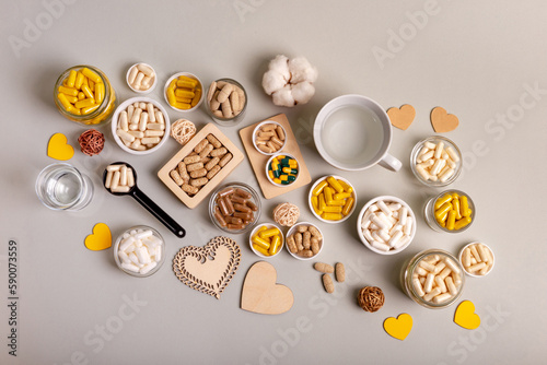 Different vitamins, minerals and food supplements in jars and a cup of water from above on light background. Nutrition supplements in form of pills, tablets and capsules to improve immune system. photo