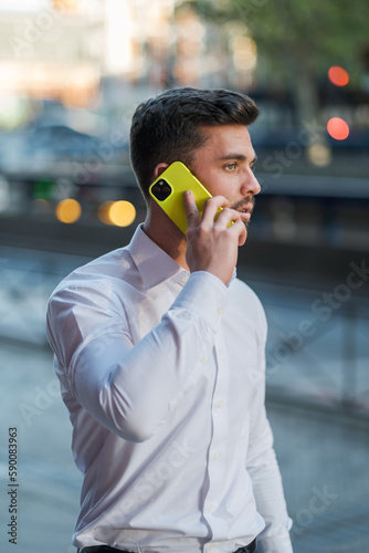 A boy in a white shirt talking on the phone with an out-of-focus background.