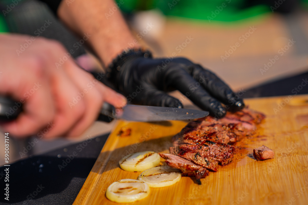 Chef with black rubber cooking gloves slicing steak on wooden board