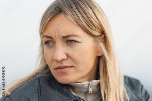 Portrait of thoughtful woman looking aside, serious woman thinking of something wearing jacket standing outdoors on cold