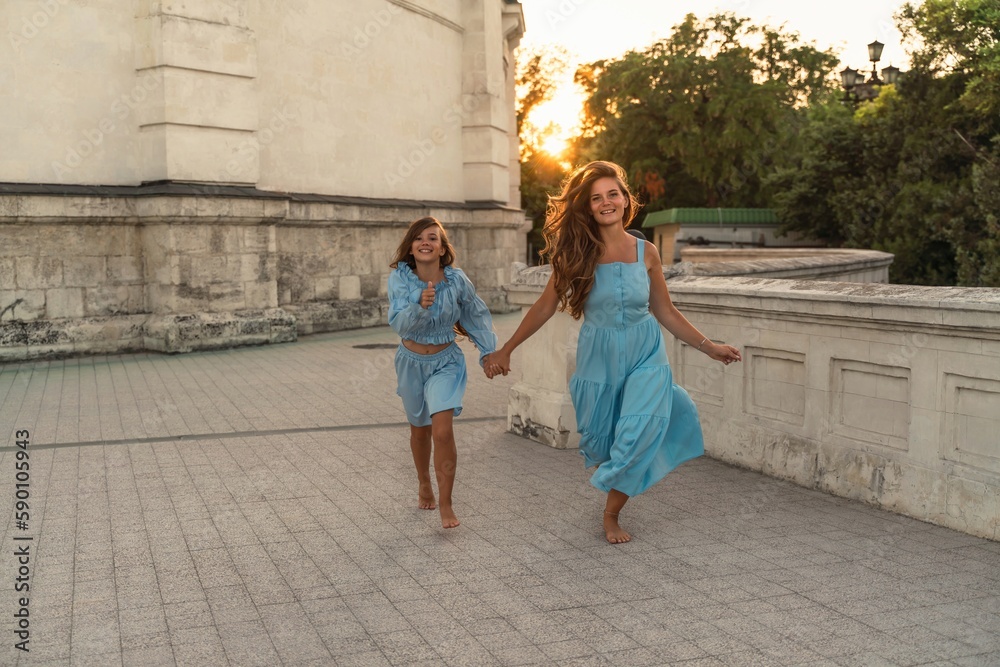 Mother daughter sunset. in blue dresses with flowing long hair against the backdrop of sunset. The woman hugs and presses the girl to her.