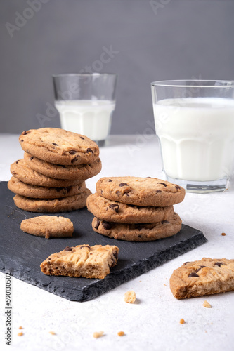 Close-up of baked oatmeal chocolate chip cookies on a slate serving board and milk in glasses. Selective focus. Vertical orientation.