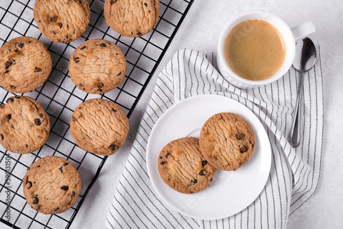 Close-up of baked oatmeal cookies with chocolate chips on a metal cooling rack and coffee in a white porcelain mug. Selective focus. photo