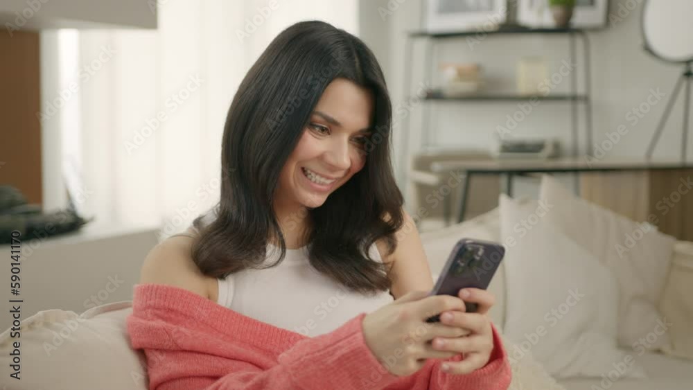 Portrait of happy beautiful woman typing in mobile phone screen indoors. Closeup cheerful girl sitting holding smartphone in loft background. Stylish smiling female holding cellphone in hands inside Portrait of happy beautiful woman typing in mobile phone screen indoors. Closeup cheerful girl sitting holding smartphone in loft background. Stylish smiling female holding cellphone in hands inside