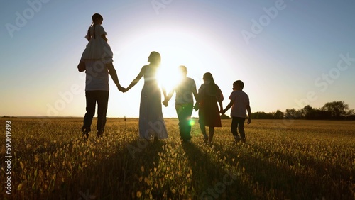 Big family in park at sunset. Group of people in nature. Family with children walk in meadow, weekend summer. Daughter on shoulders of dad, mom, son, walk hand in hand outdoors. Parental care, child