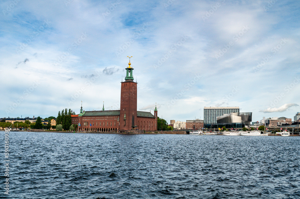 Stockholm, Sweden - Stockholm City Hall brick building with tower, waterfront with modern houses and boats.