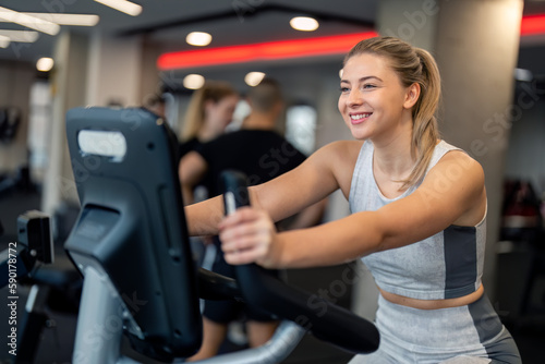 Young dedicated fit woman in good shape wearing sportswear cycling with smile on exercise bike, focused on her fitness goal, enjoying her workout cardio training day at gym fitness center.