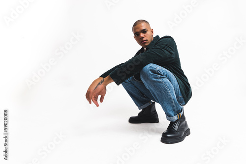 Serious male fashion model posing in squat pose and looking to the camera. Full-length studio shot. Isolated over white background. High quality photo photo