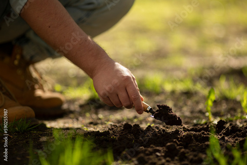 Man in jeans and yellow boots is digging hole for plant seeds with small shovel. Farmer is gardening. Summer countryside vacation. Concept of preparing for harvest, gardening. Loose soil, ground. 
