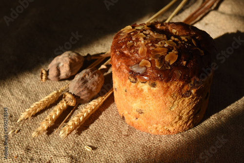 Easter cake decorated with almond is on a sacking tablecloth. Wheat spikes and poppy heads are near.Sunlight and shadows