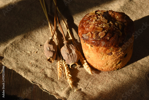Easter cake decorated with almond is on a sacking tablecloth. Wheat spikes and poppy heads are near.Sunlight and shadows