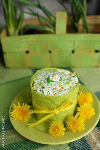 Easter Cake decorated with sugar glaze and yellow flowers on green checkered blanket. Easter picnic. Sunlight. Vertical